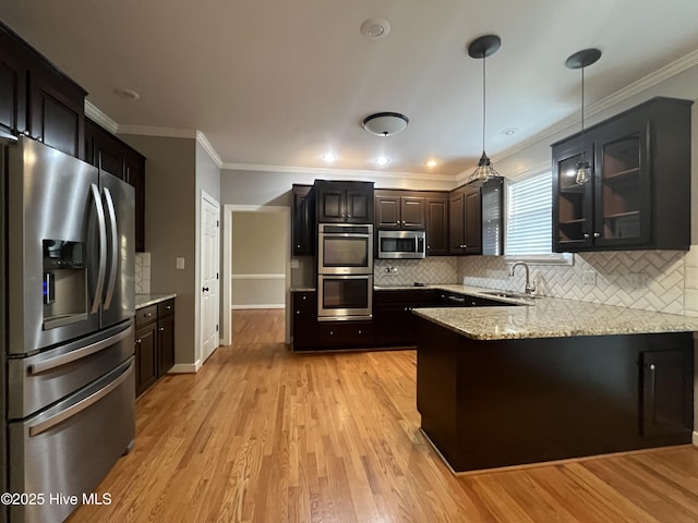 kitchen with a sink, light wood finished floors, stainless steel appliances, a peninsula, and decorative backsplash