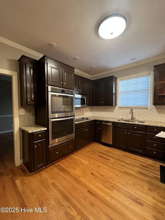 kitchen featuring crown molding, light wood-style floors, tasteful backsplash, a sink, and stainless steel appliances