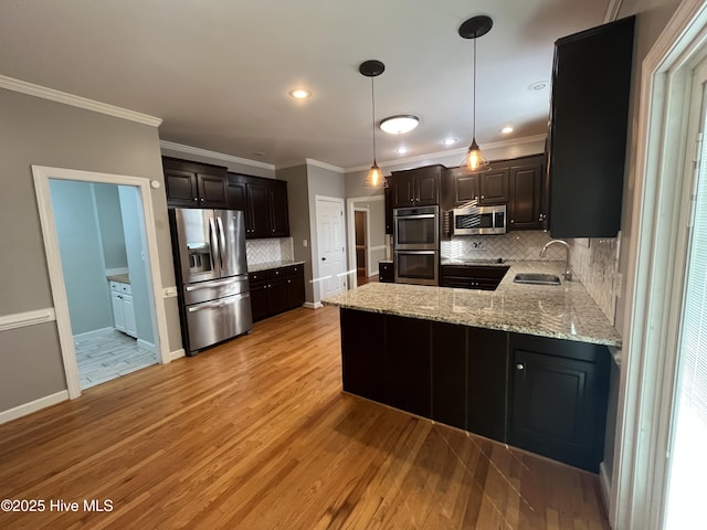 kitchen featuring a peninsula, light wood-type flooring, tasteful backsplash, a sink, and stainless steel appliances