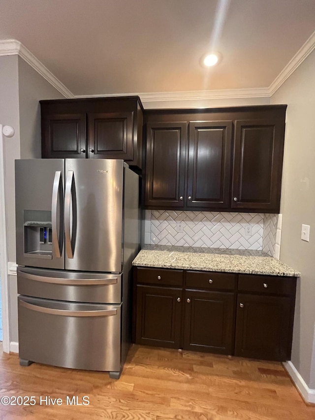 kitchen featuring decorative backsplash, dark brown cabinetry, light wood finished floors, stainless steel fridge, and ornamental molding