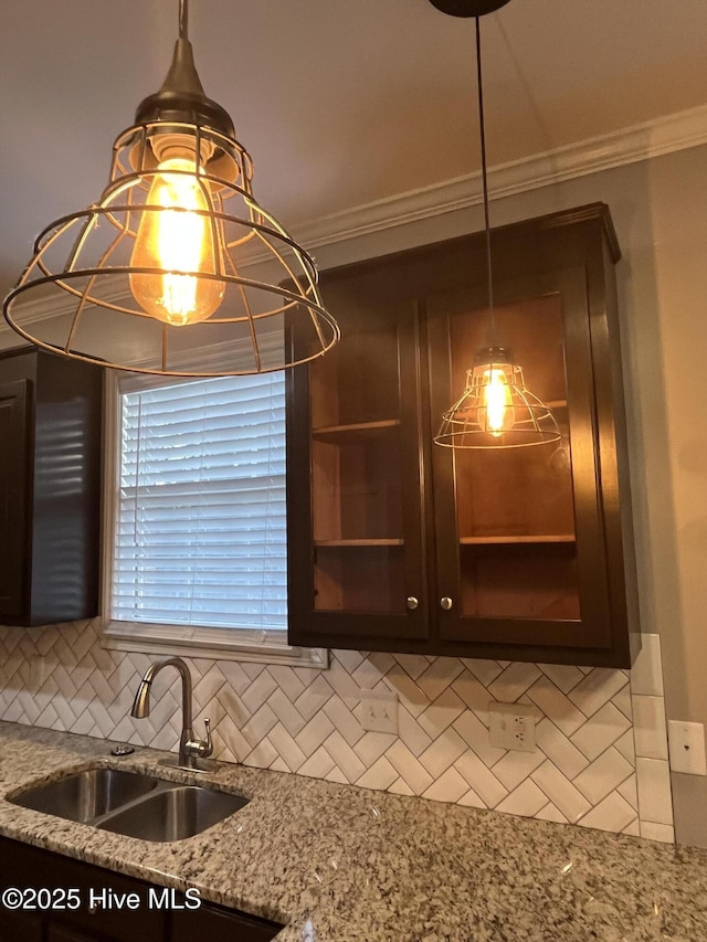 interior details featuring crown molding, dark brown cabinetry, light stone counters, a sink, and backsplash