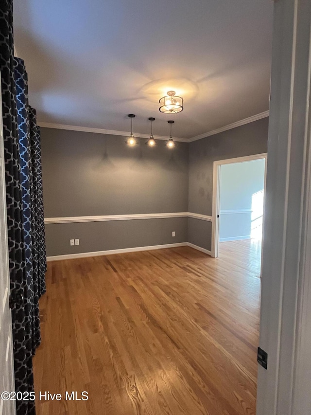 empty room featuring crown molding, baseboards, wood finished floors, and track lighting