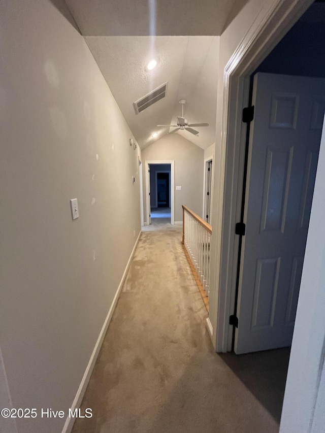hall featuring visible vents, carpet, baseboards, and vaulted ceiling