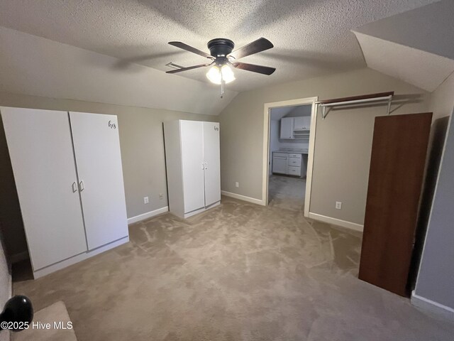 unfurnished bedroom with baseboards, ceiling fan, vaulted ceiling, and light colored carpet