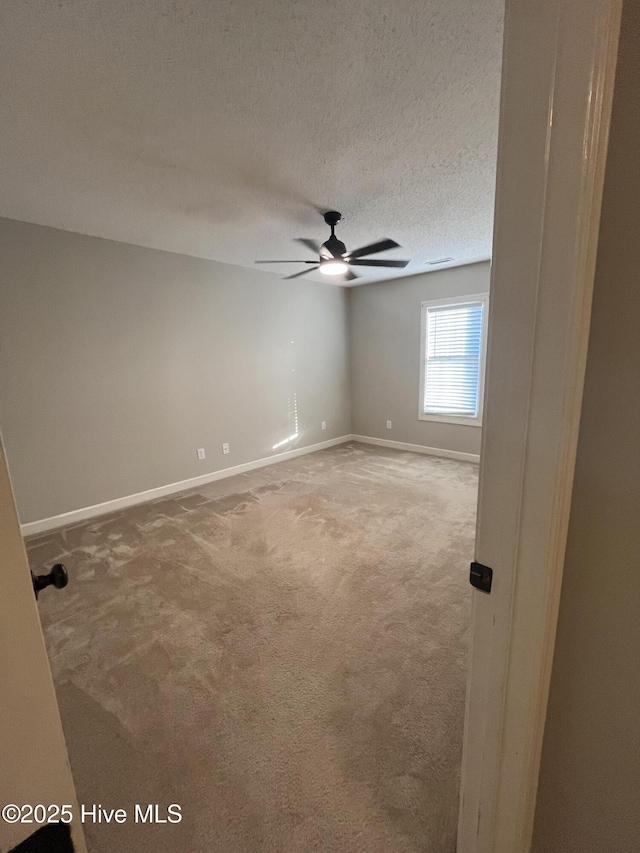 carpeted spare room featuring baseboards, a ceiling fan, and a textured ceiling