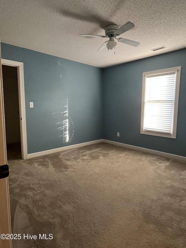 spare room with ceiling fan, a textured ceiling, carpet, baseboards, and visible vents