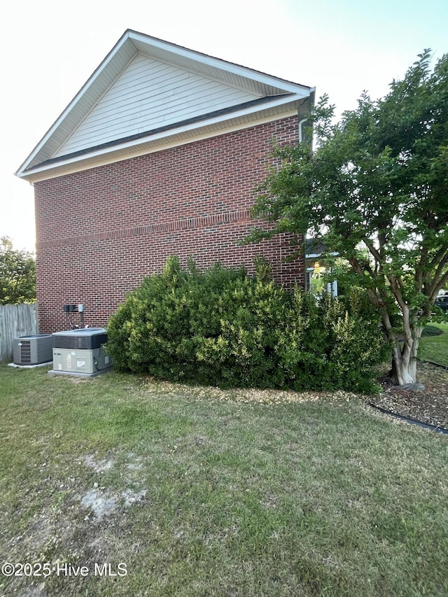 view of property exterior featuring brick siding, central AC, a yard, and fence
