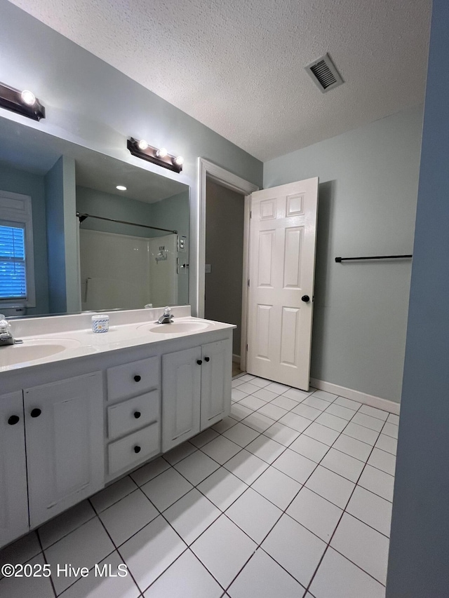 bathroom featuring visible vents, tile patterned flooring, double vanity, a textured ceiling, and a sink