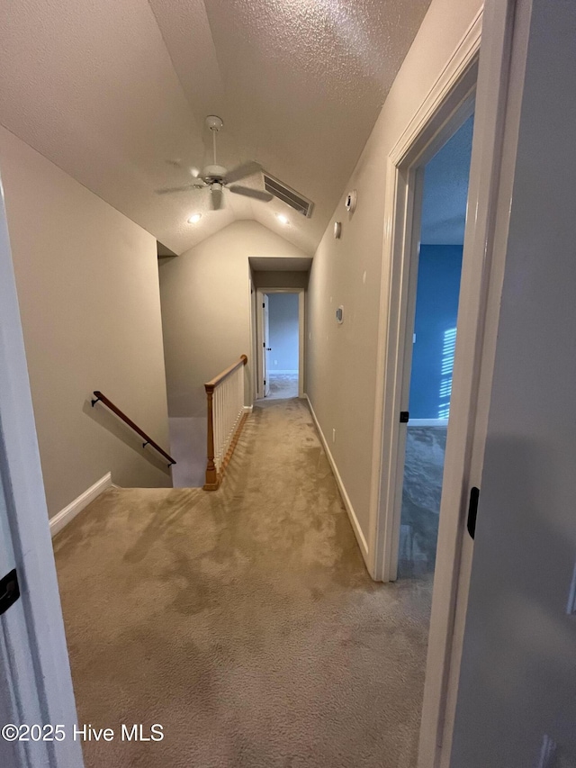 hallway with a textured ceiling, visible vents, vaulted ceiling, carpet floors, and an upstairs landing