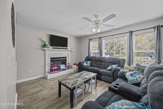 living area featuring baseboards, a ceiling fan, a glass covered fireplace, and wood finished floors