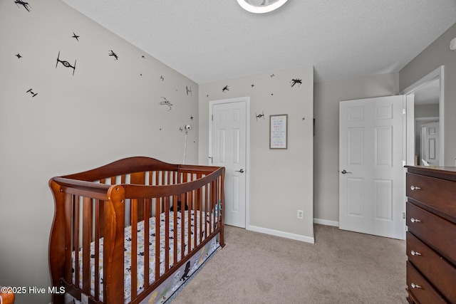bedroom featuring a textured ceiling, baseboards, a crib, and carpet