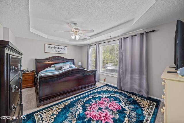 carpeted bedroom featuring baseboards, a textured ceiling, ceiling fan, and a tray ceiling