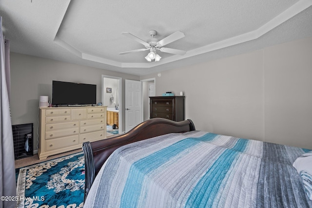 carpeted bedroom with a textured ceiling, a tray ceiling, ceiling fan, and ensuite bath