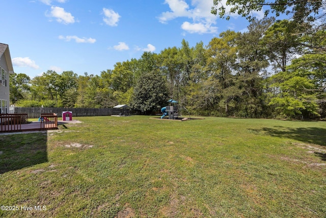 view of yard featuring a deck, fence, and a playground