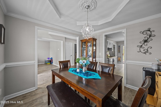 dining space featuring an inviting chandelier, ornamental molding, wood finished floors, baseboards, and a raised ceiling