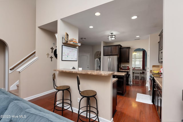 kitchen with a breakfast bar area, arched walkways, a peninsula, and appliances with stainless steel finishes