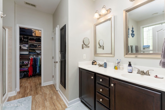 full bath featuring a spacious closet, double vanity, a sink, visible vents, and a stall shower