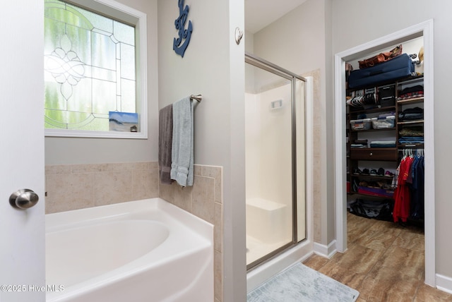 full bathroom featuring a garden tub, a stall shower, wood finished floors, and a spacious closet