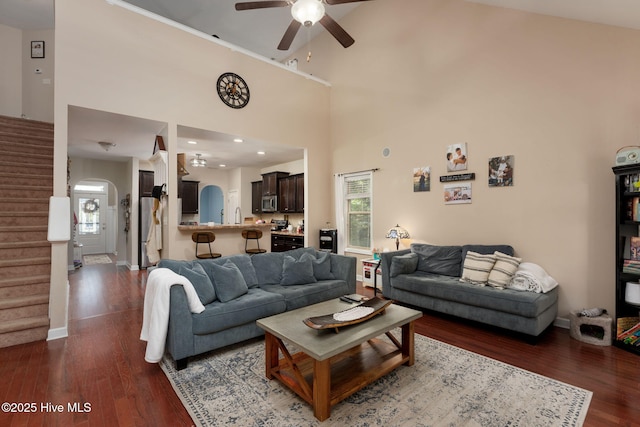 living area with arched walkways, dark wood-style flooring, baseboards, stairway, and a ceiling fan