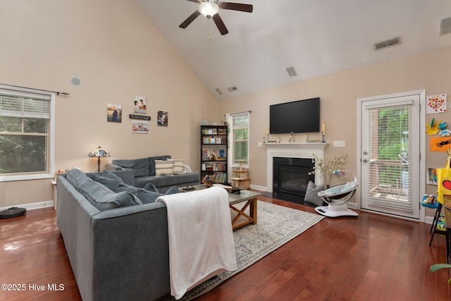 living area featuring wood finished floors, visible vents, a ceiling fan, a fireplace with flush hearth, and high vaulted ceiling