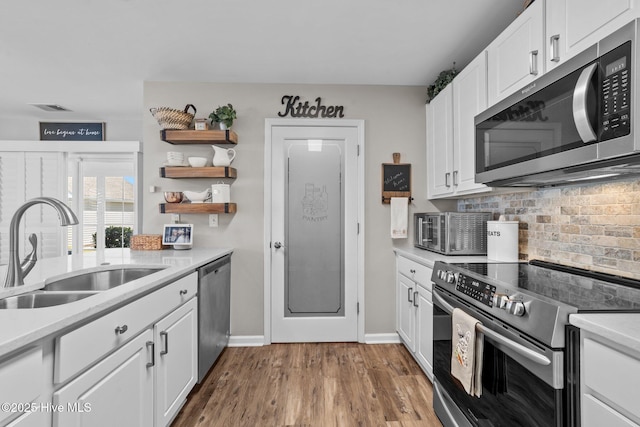 kitchen featuring open shelves, white cabinets, tasteful backsplash, a sink, and stainless steel appliances