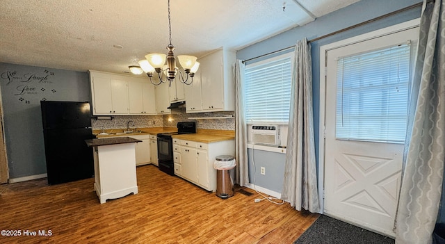 kitchen featuring a notable chandelier, under cabinet range hood, tasteful backsplash, black appliances, and white cabinets