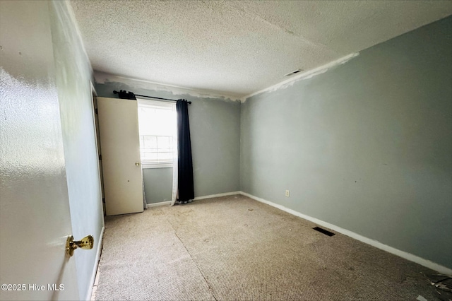 carpeted spare room featuring a textured ceiling, baseboards, and visible vents
