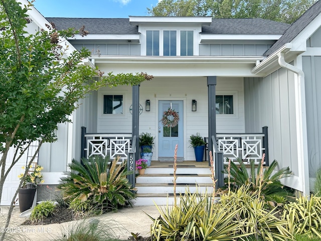 doorway to property with board and batten siding, covered porch, and roof with shingles