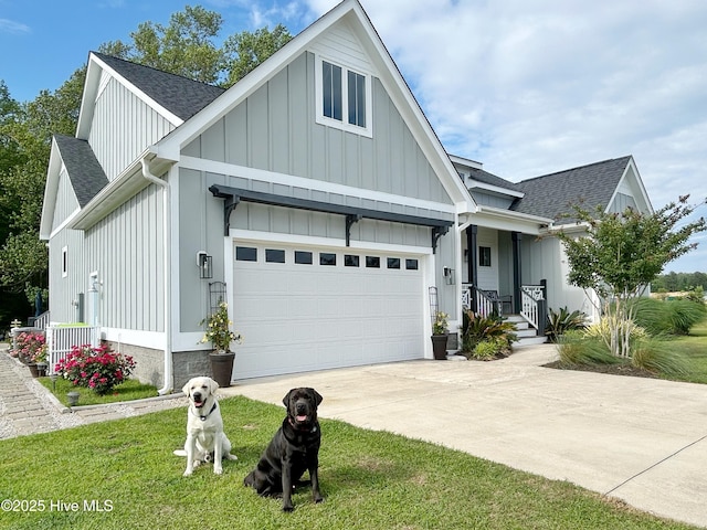 view of front facade with board and batten siding, driveway, a front yard, a garage, and a shingled roof