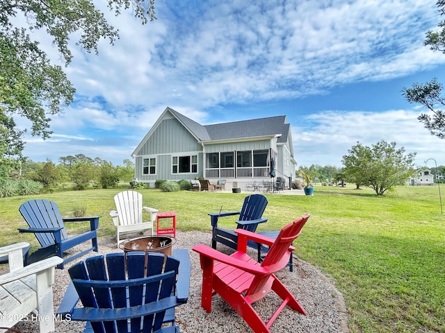 rear view of house with a sunroom, board and batten siding, an outdoor fire pit, and a yard