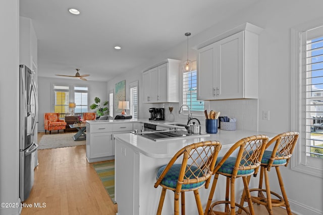 kitchen featuring a sink, a peninsula, open floor plan, stainless steel refrigerator with ice dispenser, and healthy amount of natural light