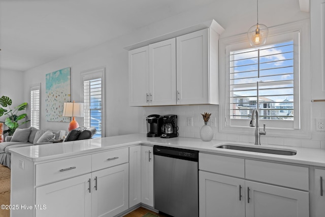 kitchen with stainless steel dishwasher, a sink, a peninsula, and decorative backsplash