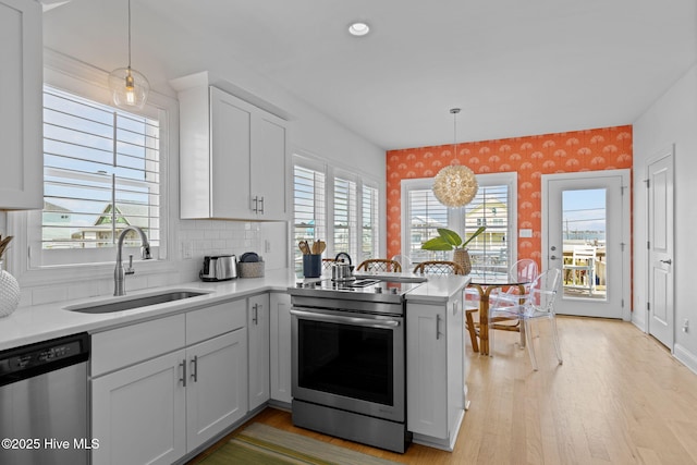 kitchen featuring appliances with stainless steel finishes, a sink, light countertops, a peninsula, and wallpapered walls