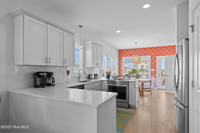 kitchen featuring appliances with stainless steel finishes, a peninsula, a sink, light countertops, and recessed lighting