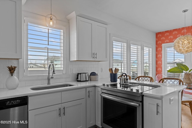 kitchen featuring stainless steel appliances, a sink, wallpapered walls, a peninsula, and white cabinets