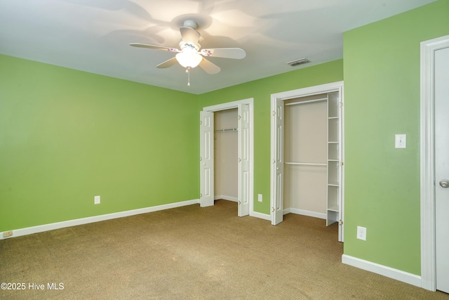 unfurnished bedroom featuring a ceiling fan, visible vents, baseboards, two closets, and carpet flooring