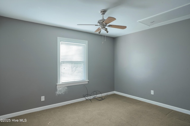carpeted empty room with a ceiling fan, baseboards, and attic access