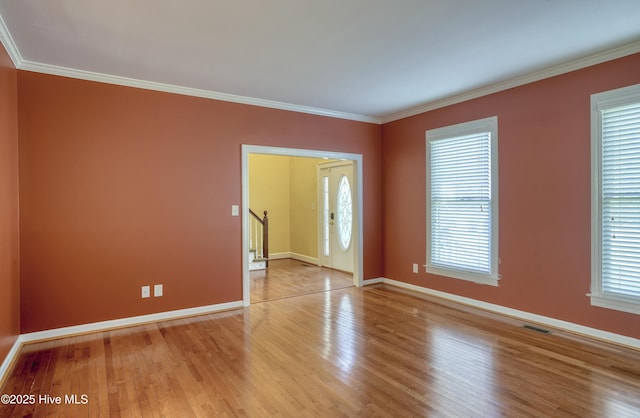 empty room with crown molding, baseboards, visible vents, and wood finished floors