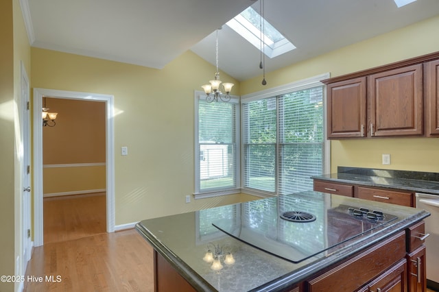 kitchen with light wood-style floors, dark stone counters, black electric cooktop, vaulted ceiling with skylight, and a notable chandelier