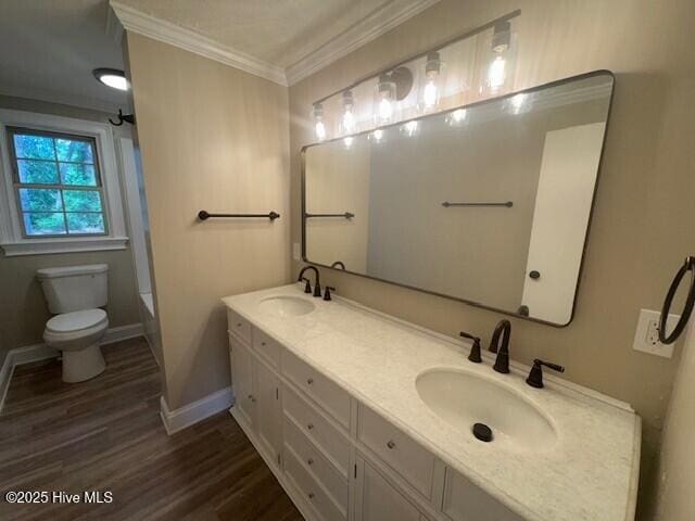 bathroom with wood finished floors, toilet, ornamental molding, and a sink