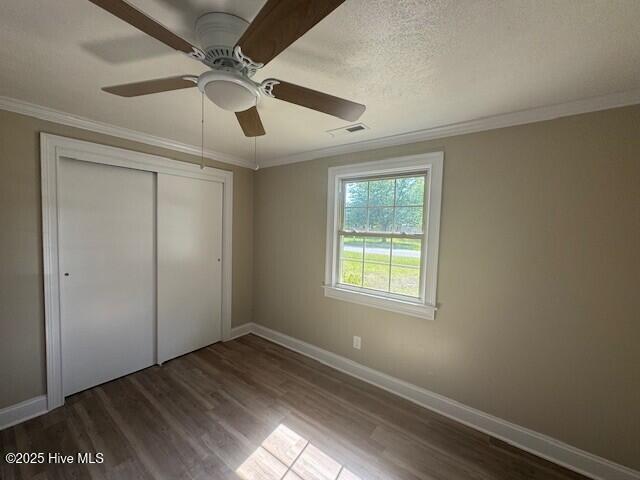 unfurnished bedroom with dark wood-style floors, crown molding, visible vents, and a closet