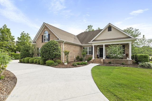 craftsman-style home featuring a porch, driveway, roof with shingles, brick siding, and a front lawn