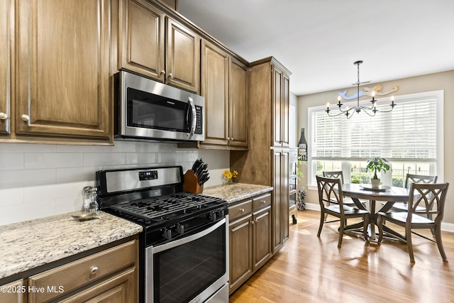 kitchen featuring appliances with stainless steel finishes, light stone counters, an inviting chandelier, light wood-style floors, and tasteful backsplash