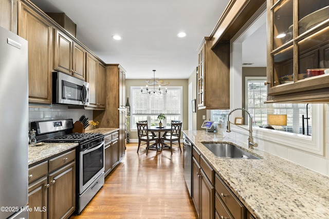 kitchen with appliances with stainless steel finishes, light stone countertops, a sink, a notable chandelier, and a wealth of natural light