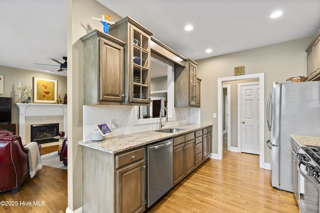 kitchen featuring a sink, a glass covered fireplace, light wood-style flooring, stainless steel appliances, and a ceiling fan