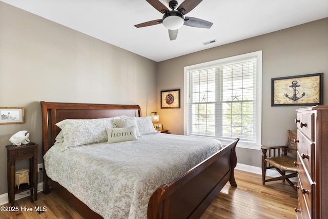 bedroom with baseboards, a ceiling fan, wood finished floors, and visible vents