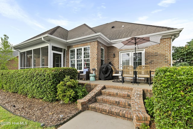 back of property featuring a sunroom, a shingled roof, a patio area, and brick siding