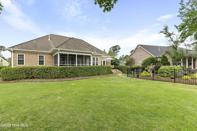 back of property featuring a yard, brick siding, fence, and a sunroom