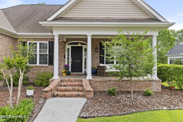 property entrance with covered porch, brick siding, and roof with shingles