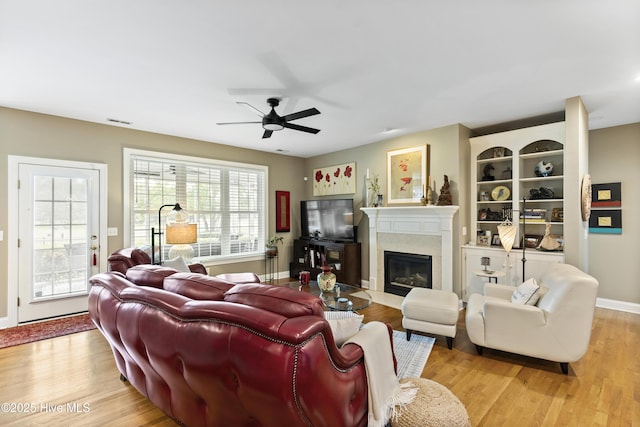 living area featuring a premium fireplace, a ceiling fan, baseboards, light wood-type flooring, and visible vents